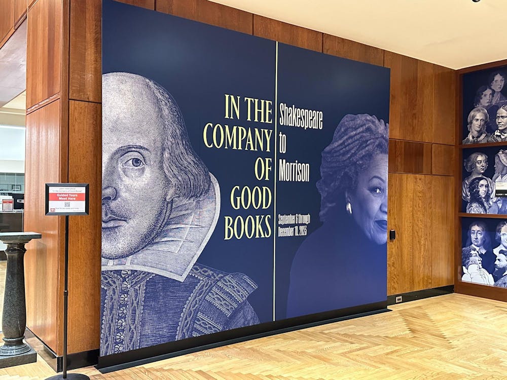 The sign for the exhibition in the first floor of Firestone. The sign is colored navy blue. On the left half is half of Shakespeare's face along with the words "In the Company of Good Books," and the right shows half of Toni Morrison's face with the words "Shakespeare to Morrison: September 6 through December 10, 2023." 