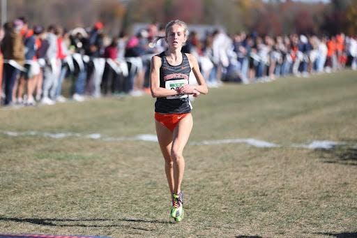 Girl in black and orange cross-country uniform crosses the finish line