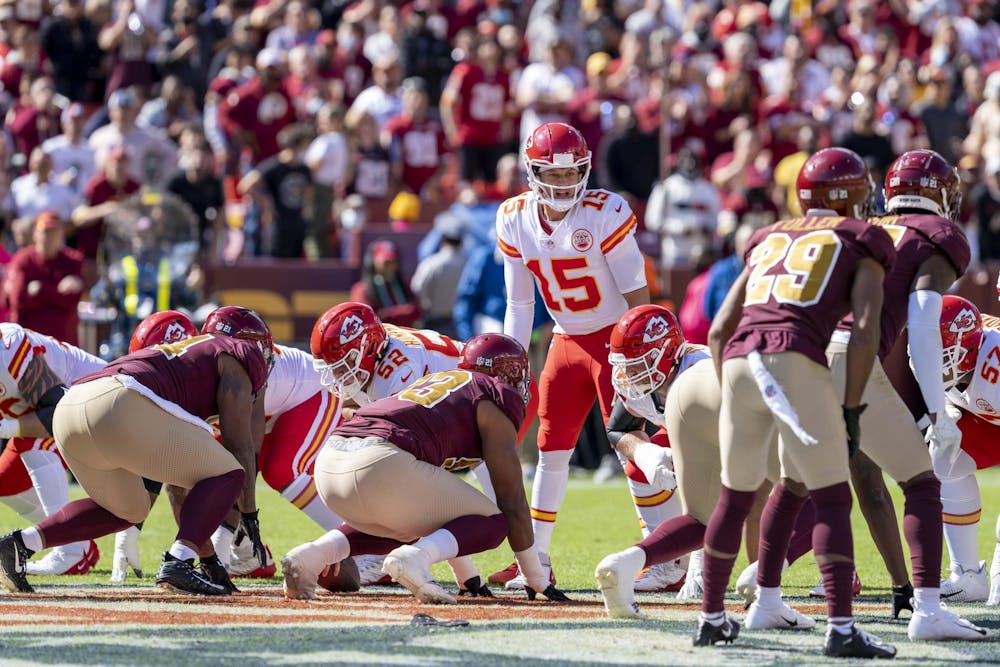 Player wearing 15 jersey in Kansas City Chiefs red and white uniform gets ready to snap the ball in a game against the Washington Commanders.