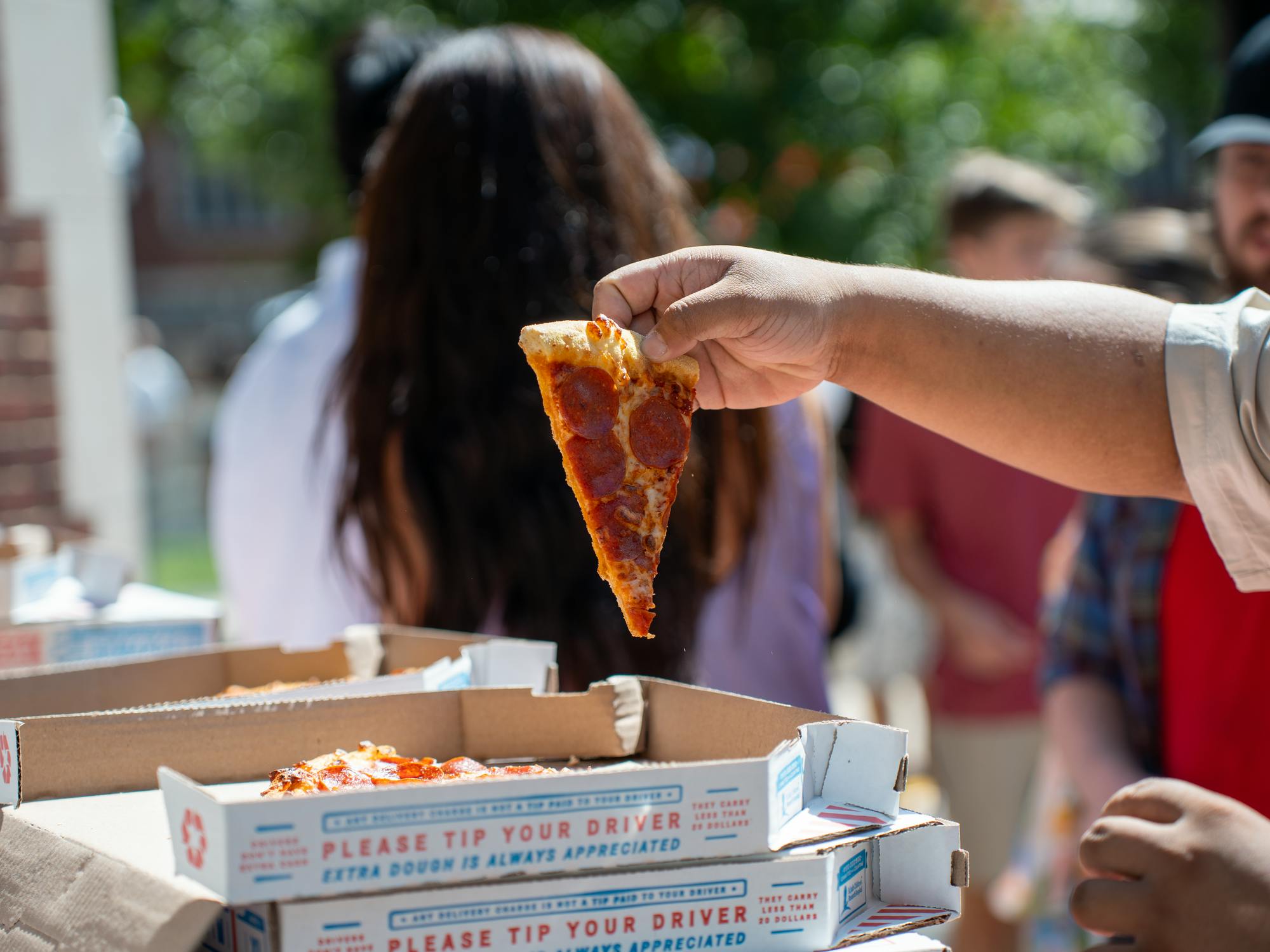 A hand holds a slice of pepperoni pizza aloft.