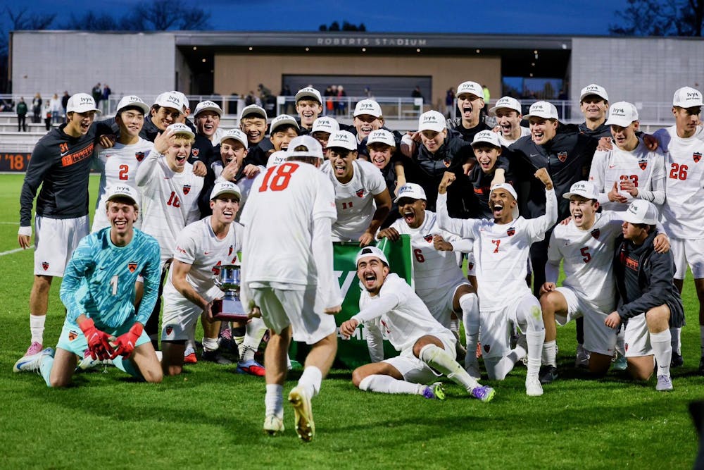 A group of soccer athletes wearing white shorts, white jerseys, and customized hats, celebrating a title on a grass field.