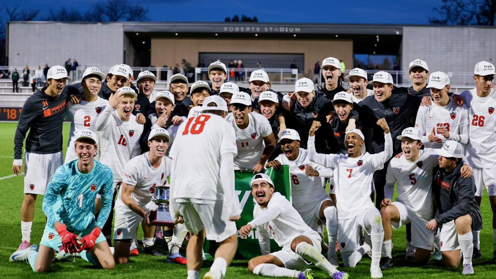 A group of soccer athletes wearing white shorts, white jerseys, and customized hats, celebrating a title on a grass field.