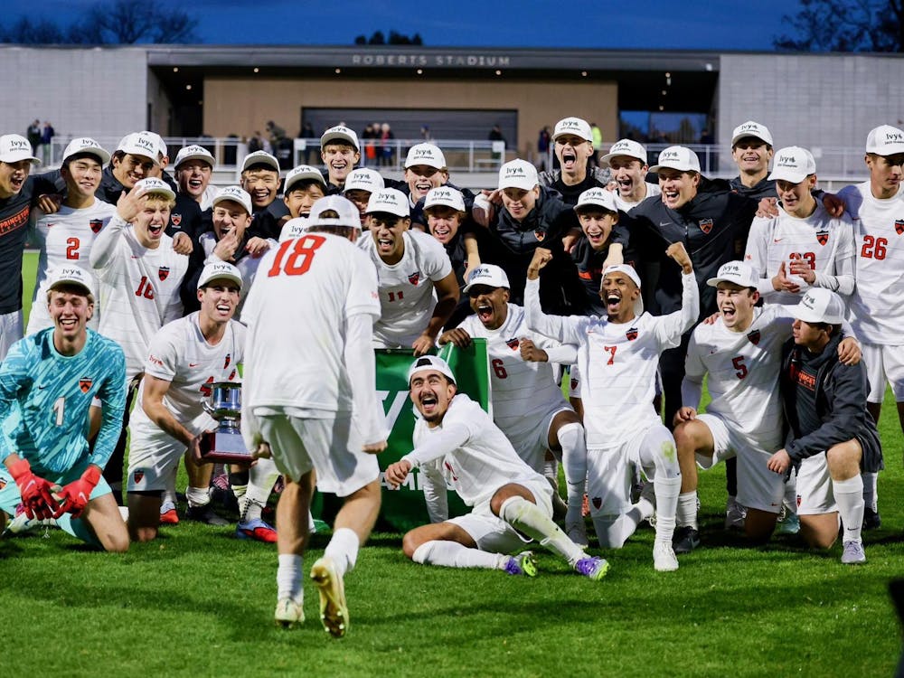A group of soccer athletes wearing white shorts, white jerseys, and customized hats, celebrating a title on a grass field.