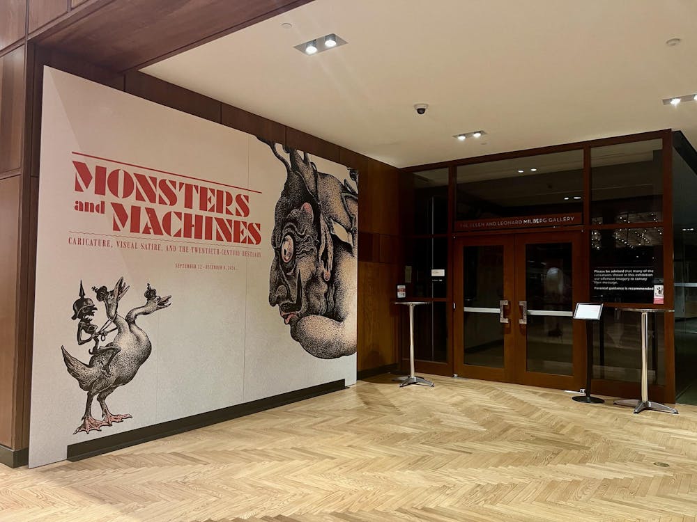 A large horizontal poster with large red letters saying "Monsters and Machines" and images of monsters rests along a wall next to an exhibition.