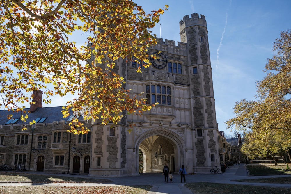 Fall leaves on a tree are in front of a gothic building with a large arch at the center.