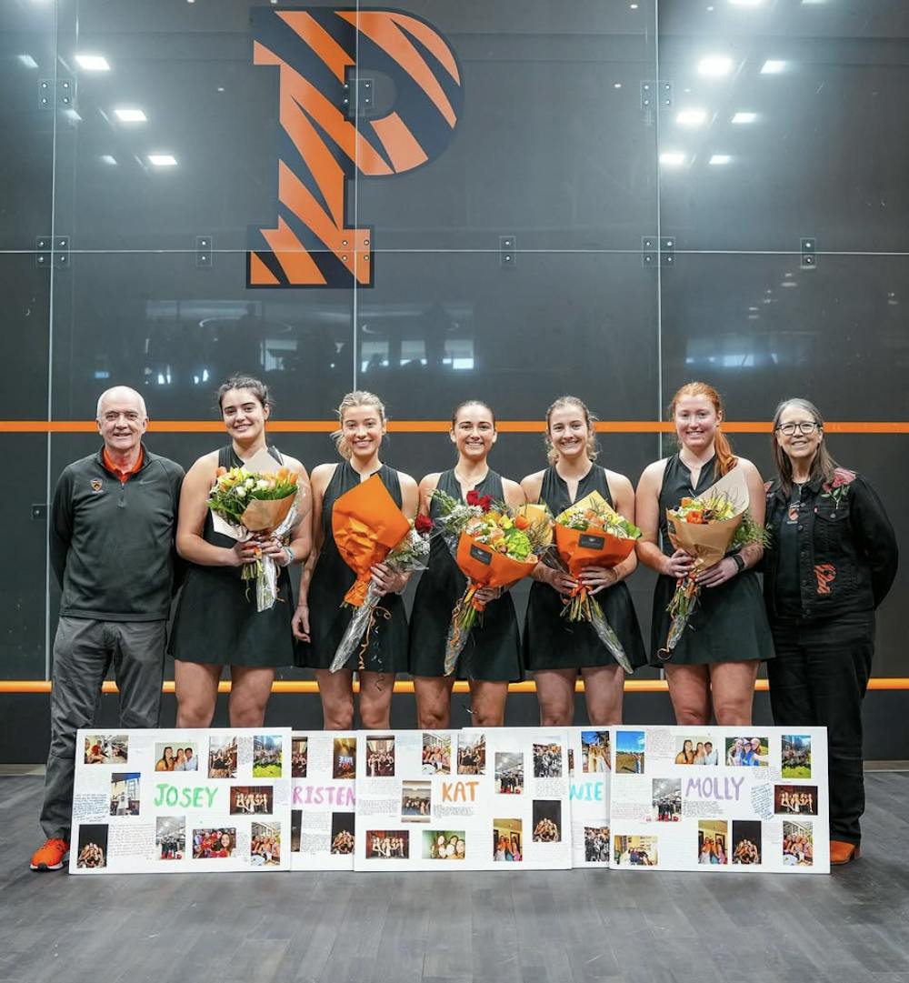 Squash players and coaches standing with flowers in front of squash court.