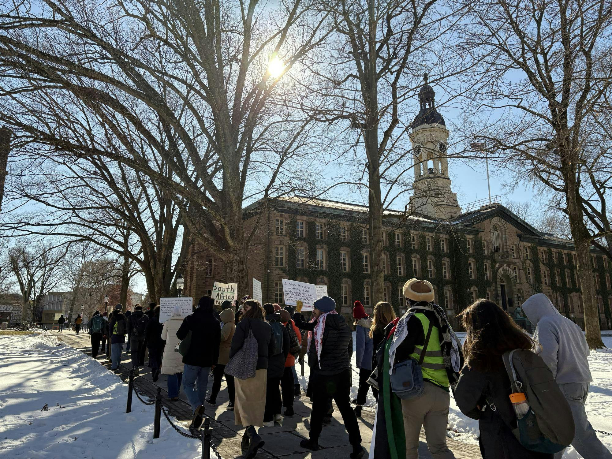 Students holding signs rally outside of ivy-covered building.