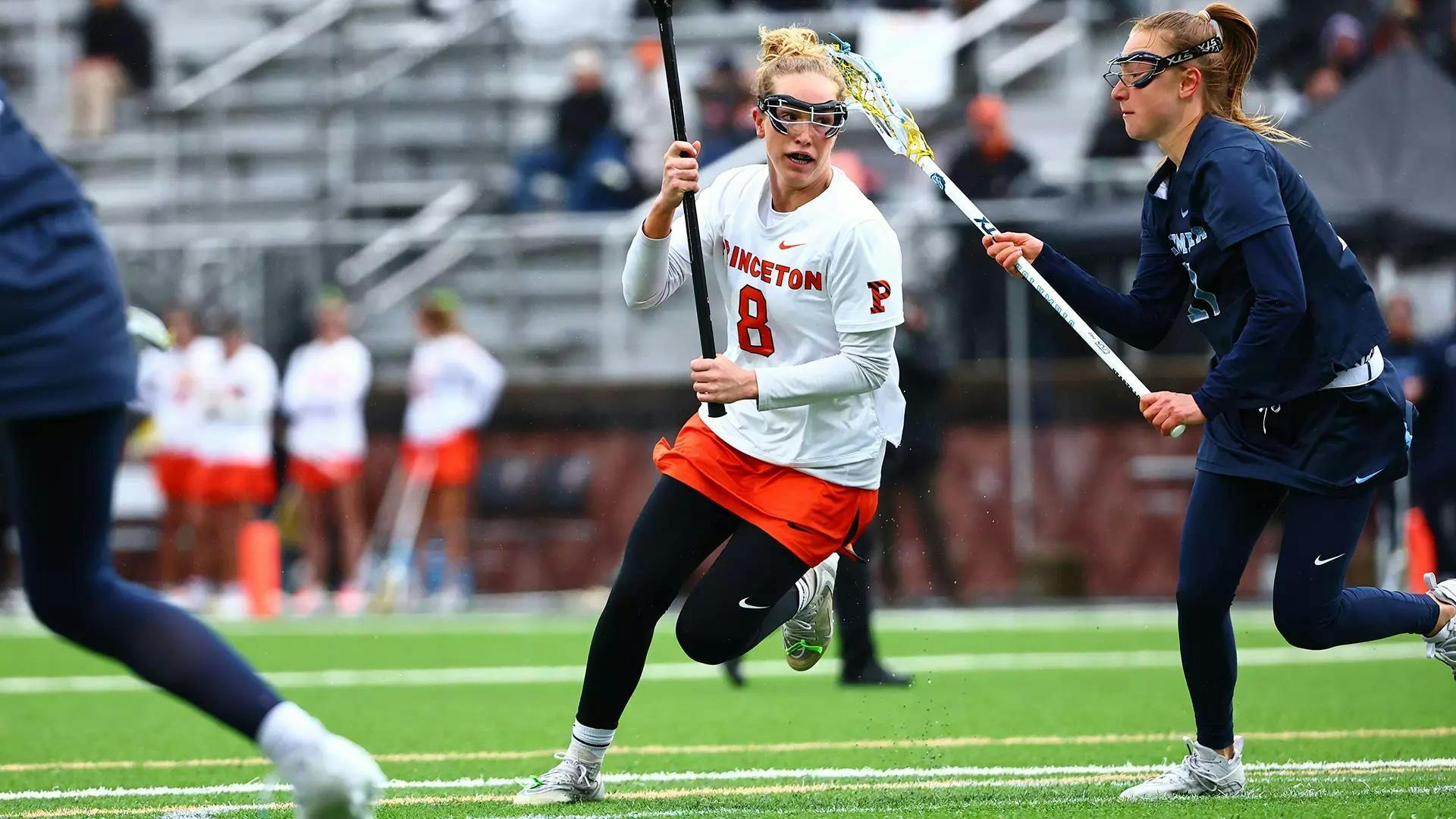 A woman on a field holding a stick as she looks to score a goal during a lacrosse game.