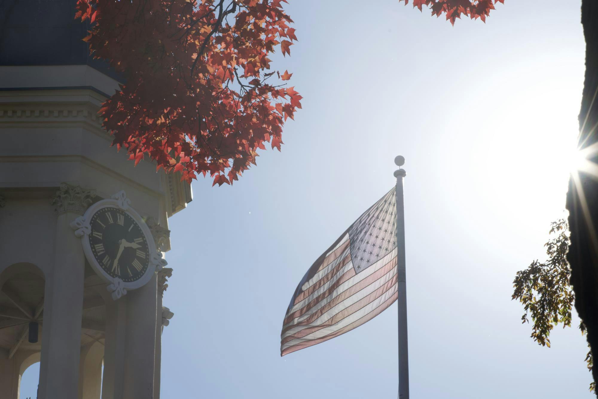 American flag flies on a sunny day next to a tan bell tower.