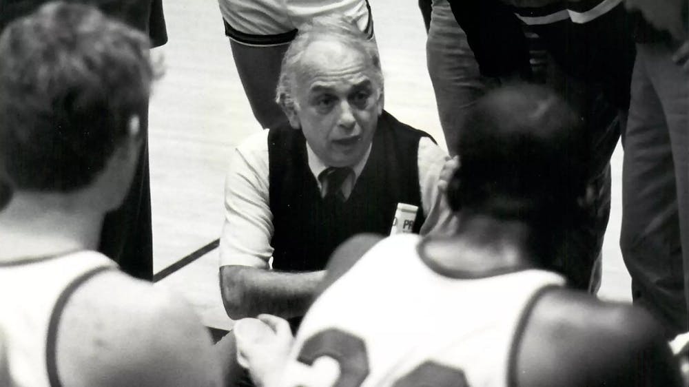 Black and white image of man crouching with basketball players surrounding him.