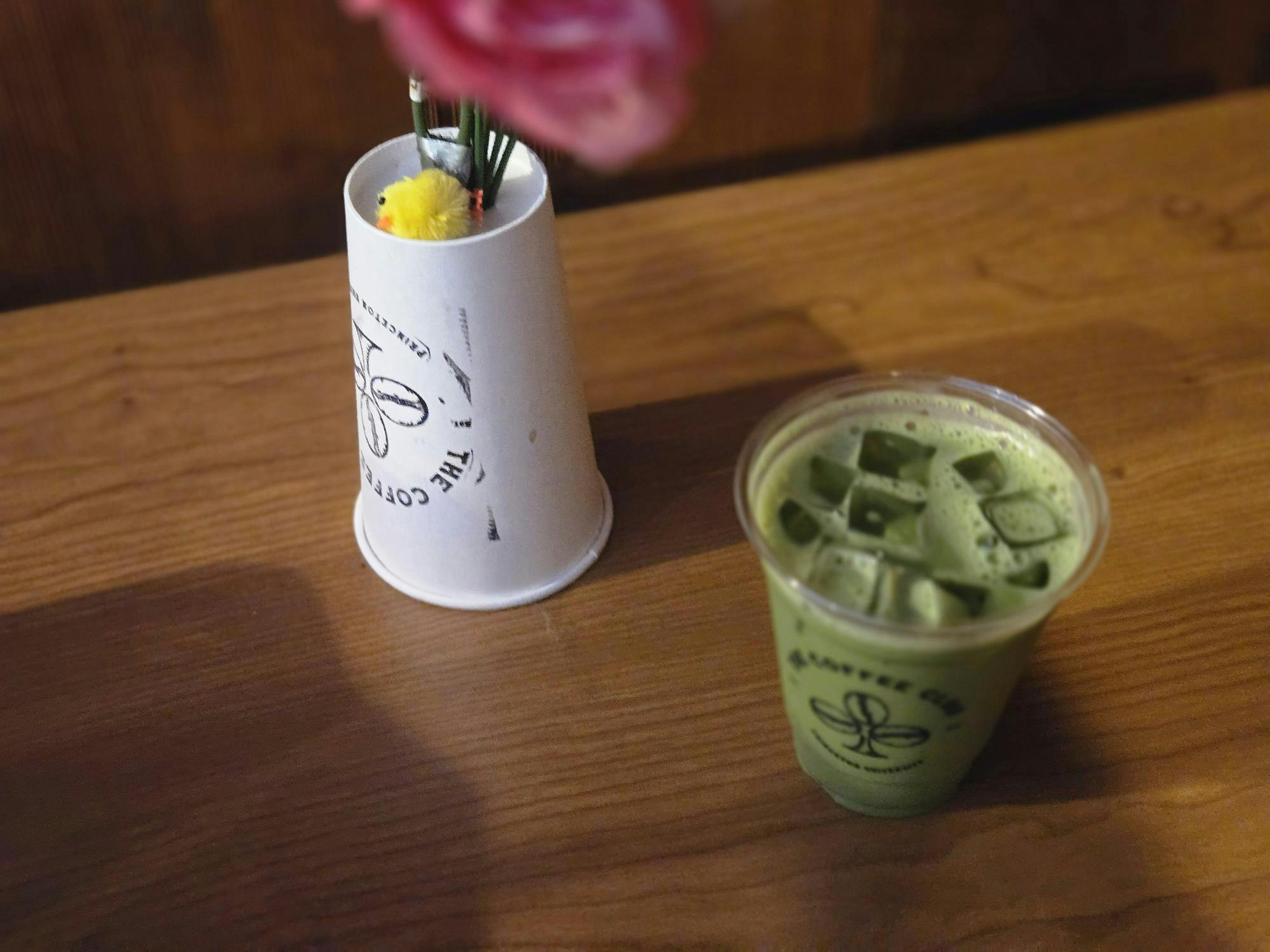 A green drink in a transparent cup and a white Coffee Club cup that is upside down sit on a brown table.