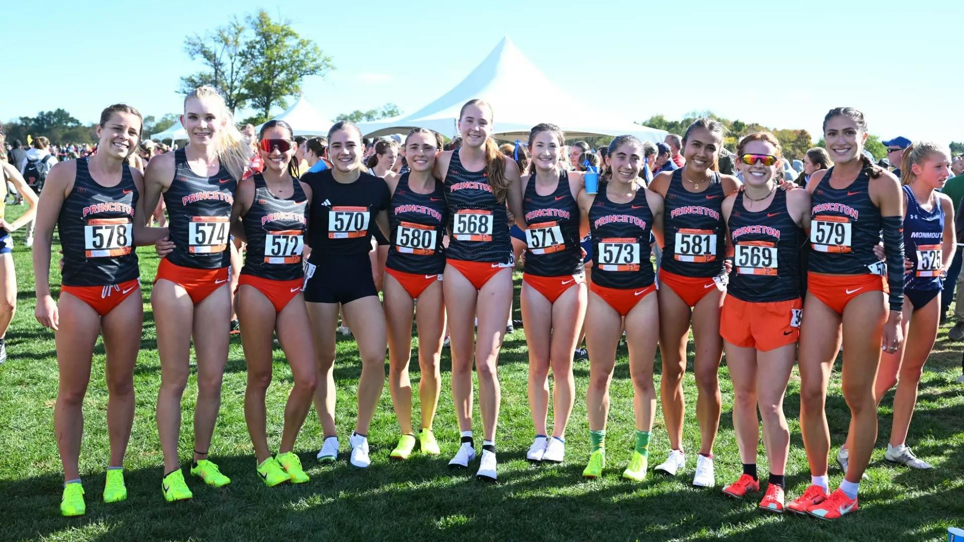 Women in black running shirts and orange shorts line up for a photo.