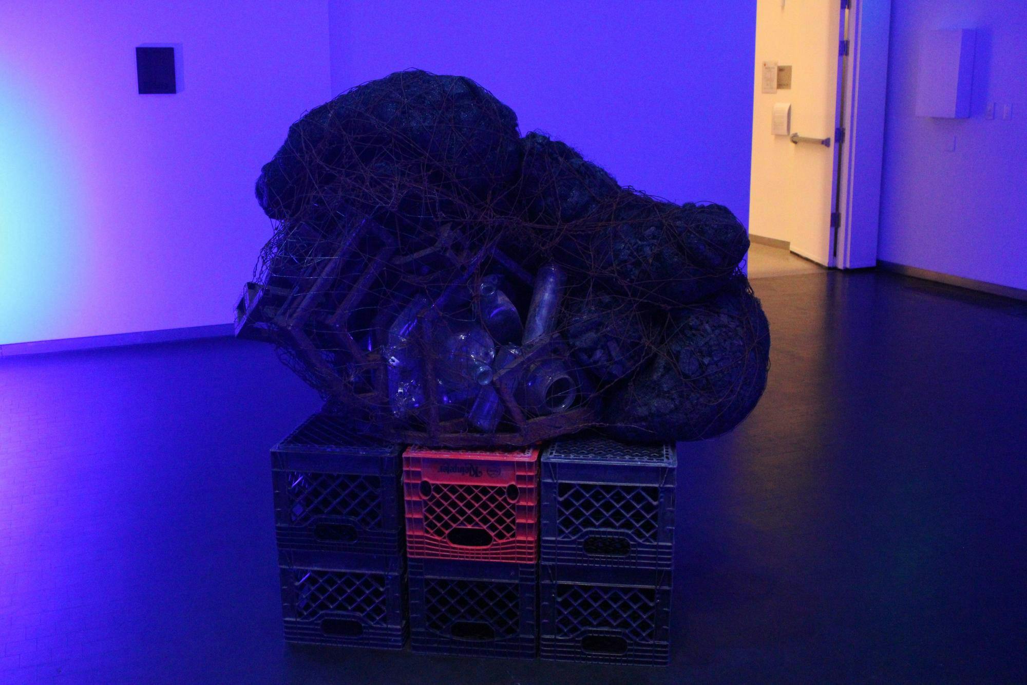 On top of a box of plastic cartons sits a bag of empty water bottles all strung together within black netting. 