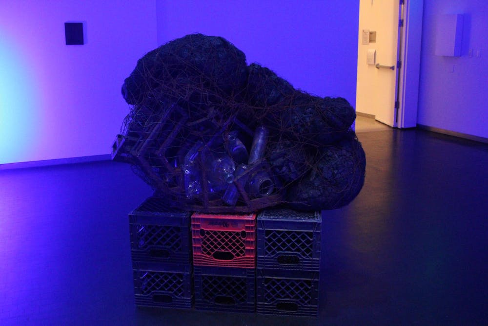 On top of a box of plastic cartons sits a bag of empty water bottles all strung together within black netting. 