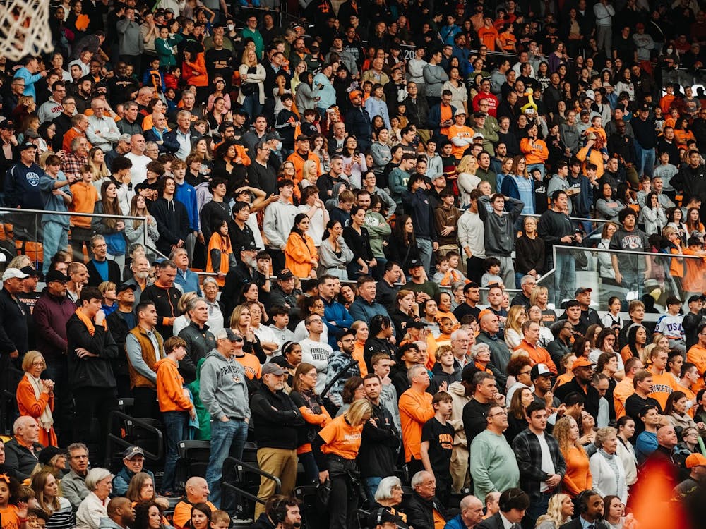 A large gathering of fans wearing mostly black and orange sit in the lower tier of the Jadwin Gymnasium stands.