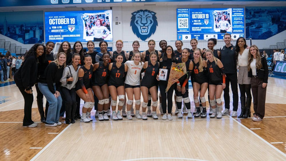 A group of men and women pose and celebrate their coach who is holding flowers on a court inside a gym. 