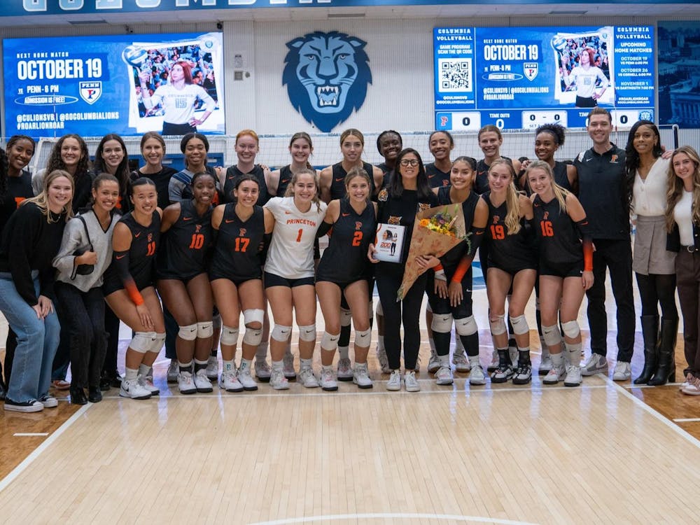 A group of men and women pose and celebrate their coach who is holding flowers on a court inside a gym.