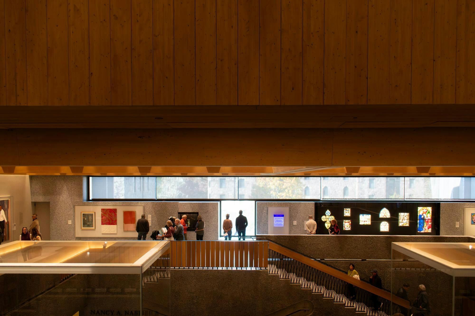 A downward view of people looking at a wall of art, including paintings and stained glass. 