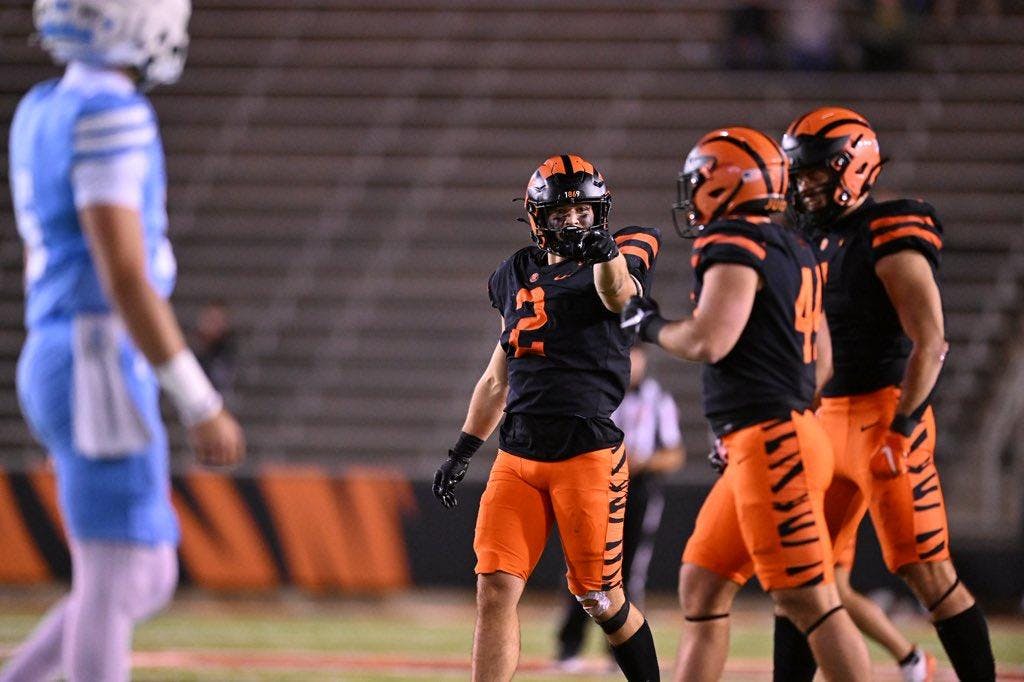 Three Princeton players in black and orange uniforms walk on field.