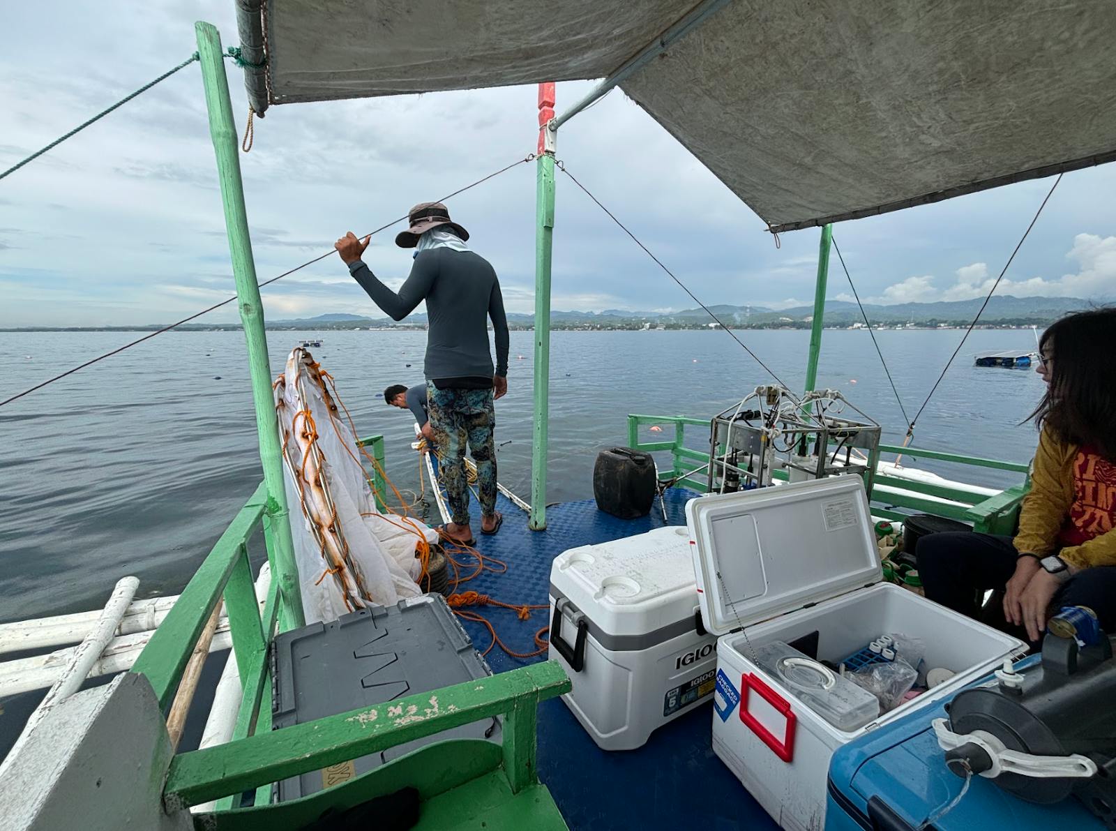 There are three people on a boat. One is leaning over, gathering seaweed from the sea.