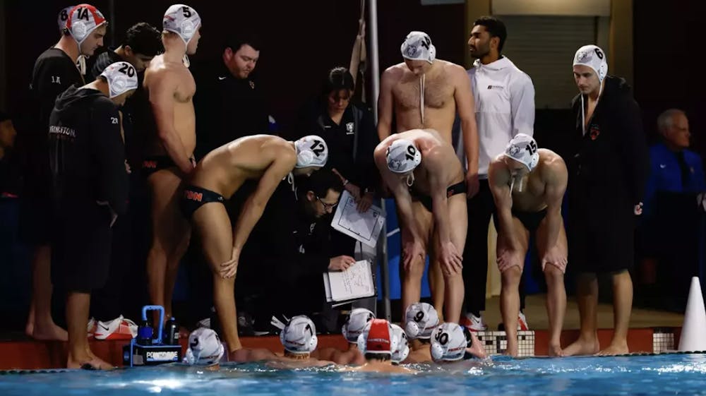Water polo athletes huddle around a man pointing at a white clipboard.