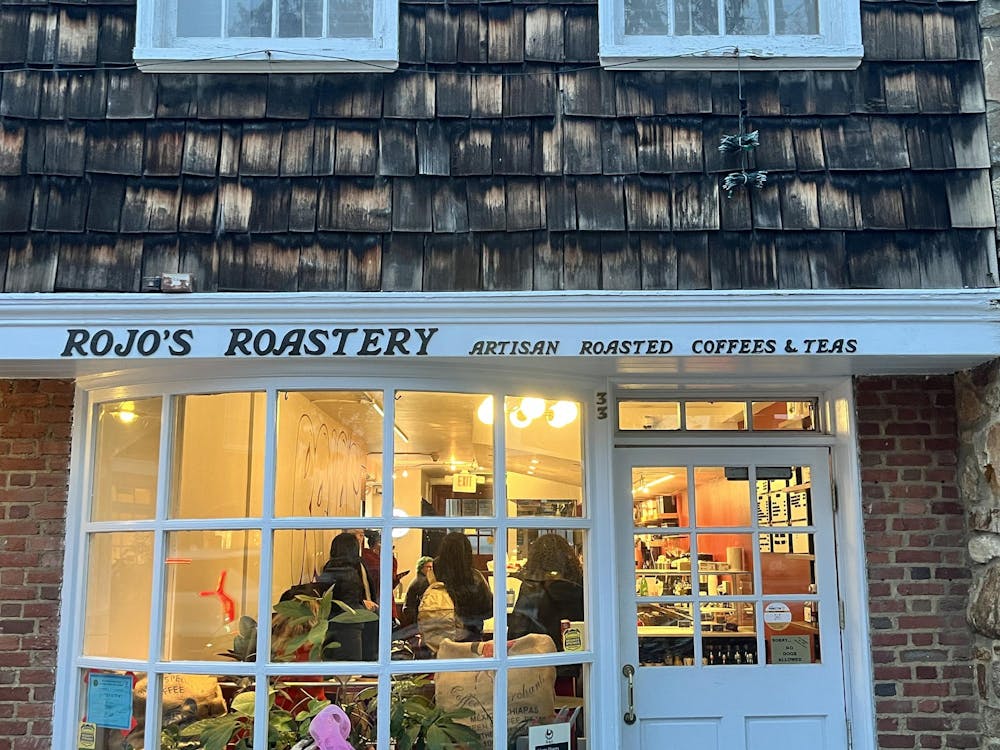 Front view of a coffee shop with people inside. On the white trim, it says "Rojo's Roastery Artisan Roasted Coffees & Teas."