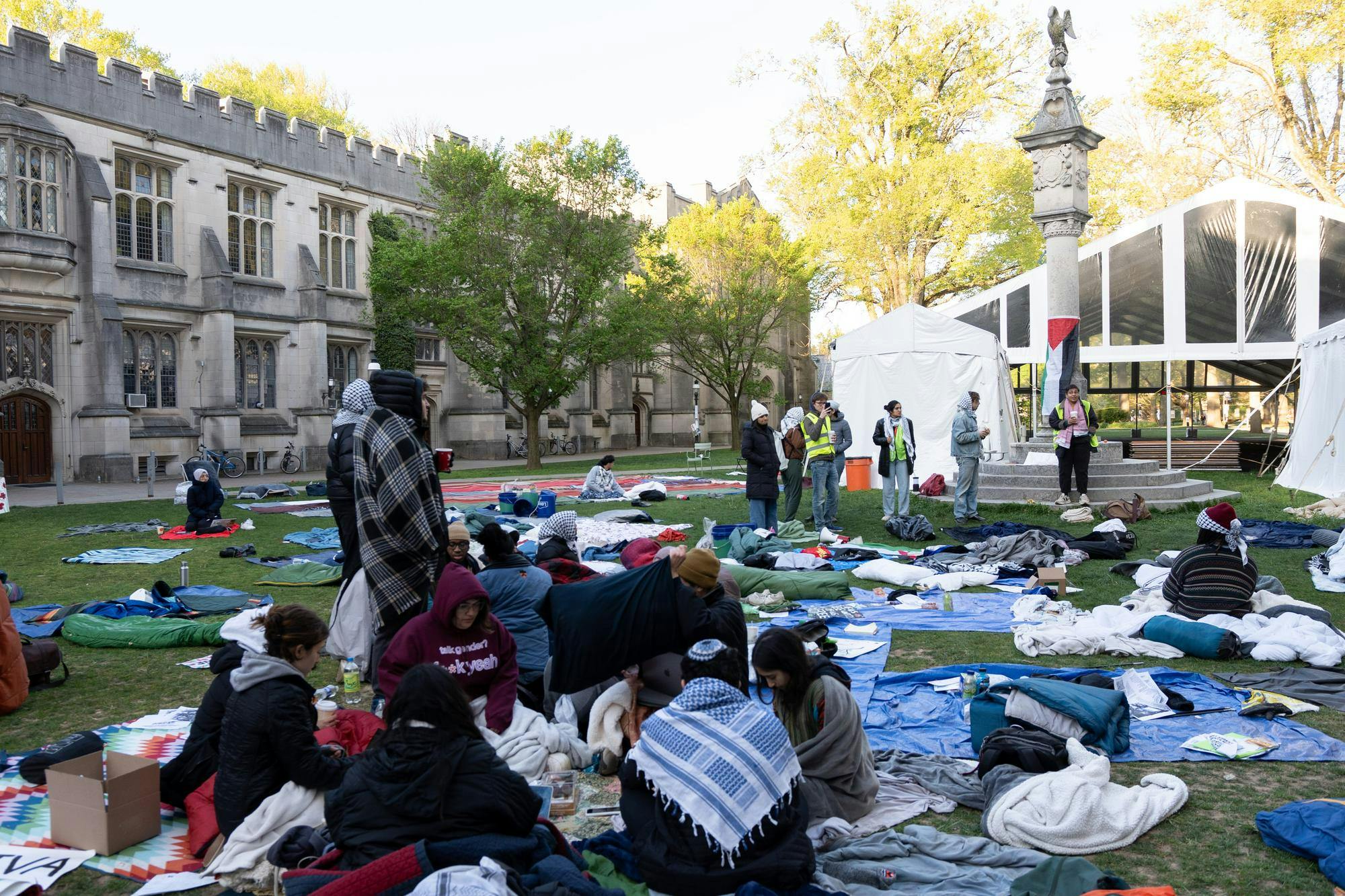 Student protestors sit on a lawn in the early morning with blankets strewn around them.