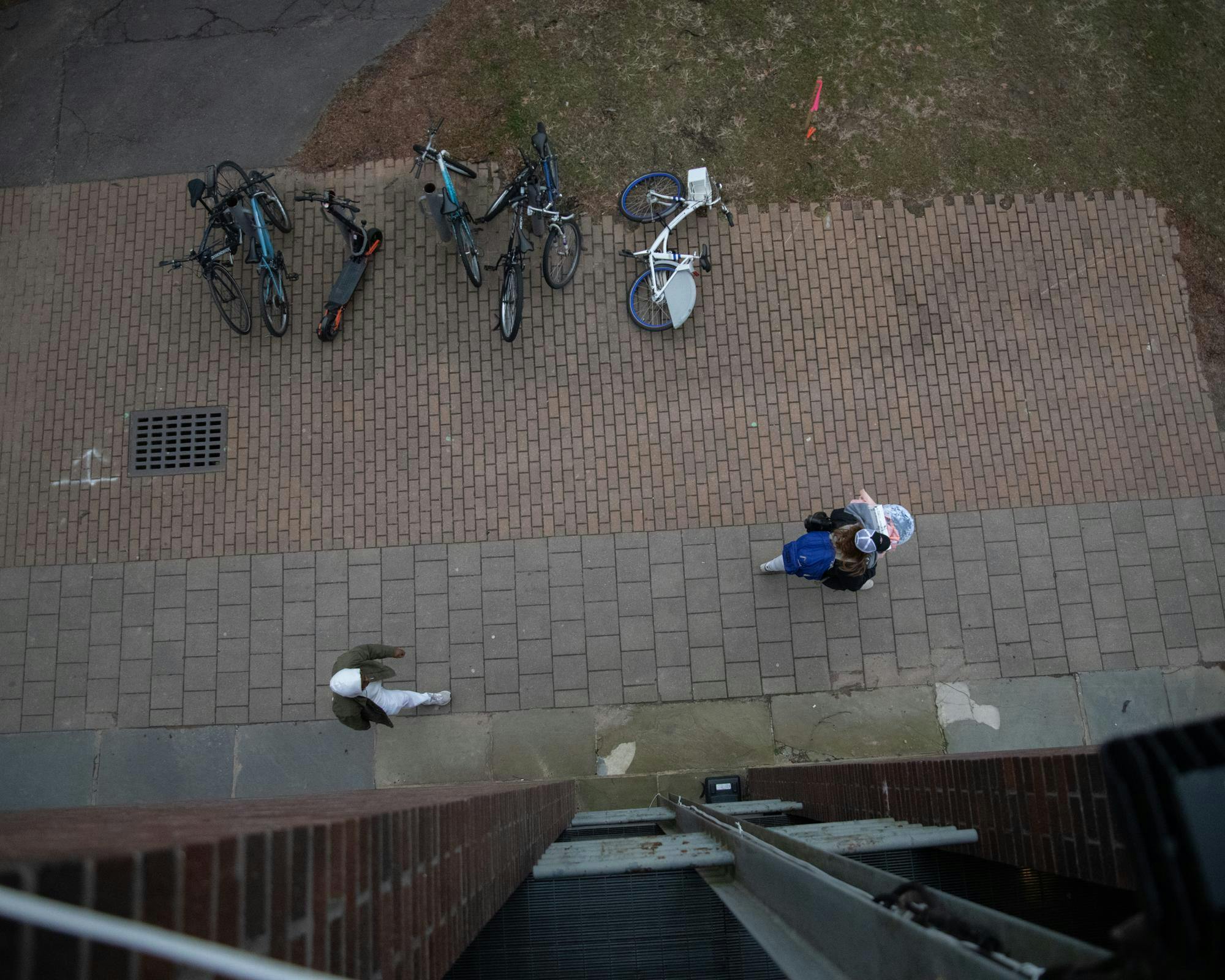 Two students walk on the sidewalk near locked bikes, pictured from directly overhead.