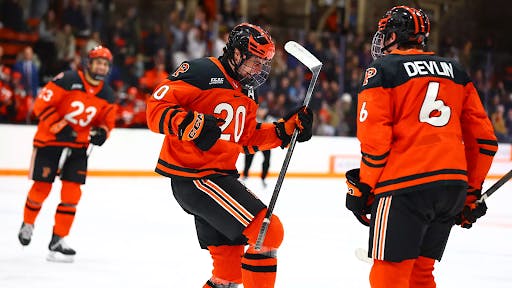 Hockey players in orange jerseys celebrate a goal.