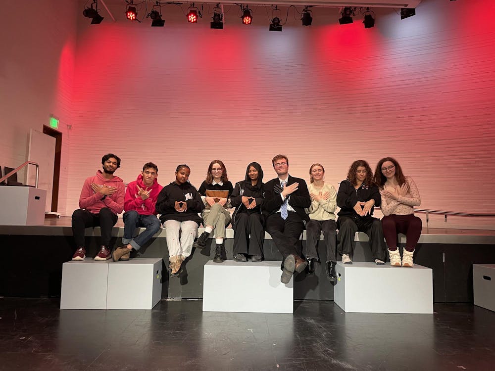 A group of people sit in a line on stage in front of red lighting.