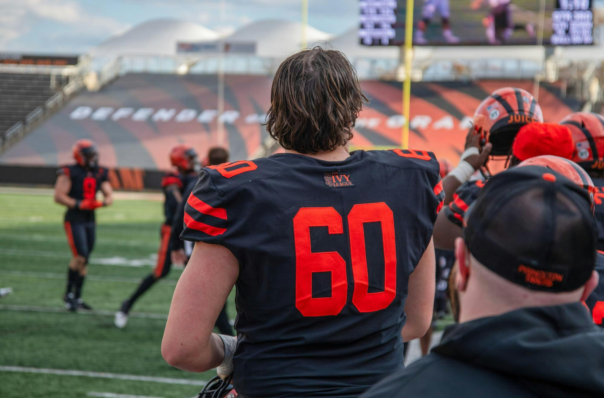 A football player in Princeton colors with the number 80 watches the scoreboard.