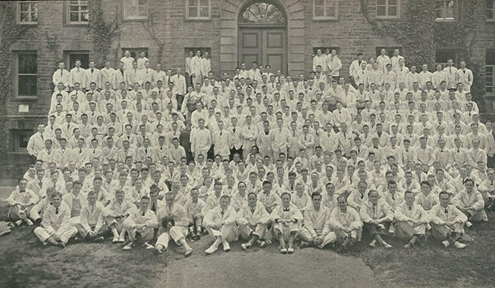 Men gathered in front of Nassau Hall in white jackets, pictured in black and white.