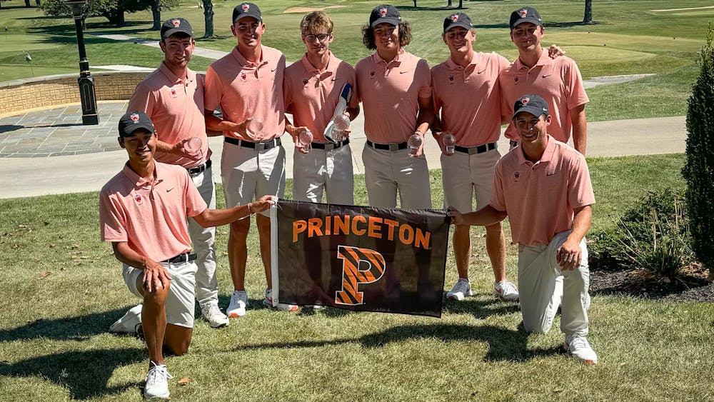 Group of men in orange shirts pose on a golf course with a banner. 