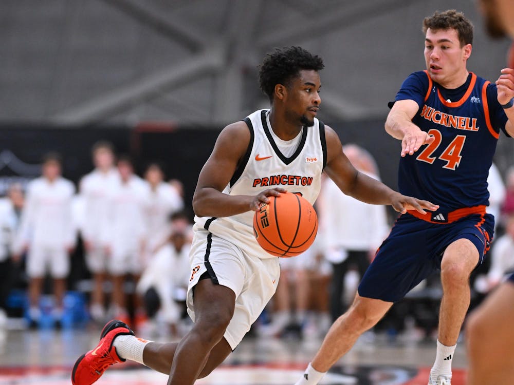 Princeton basketball player in white jersey dribbles basketball past player in navy blue jersey.