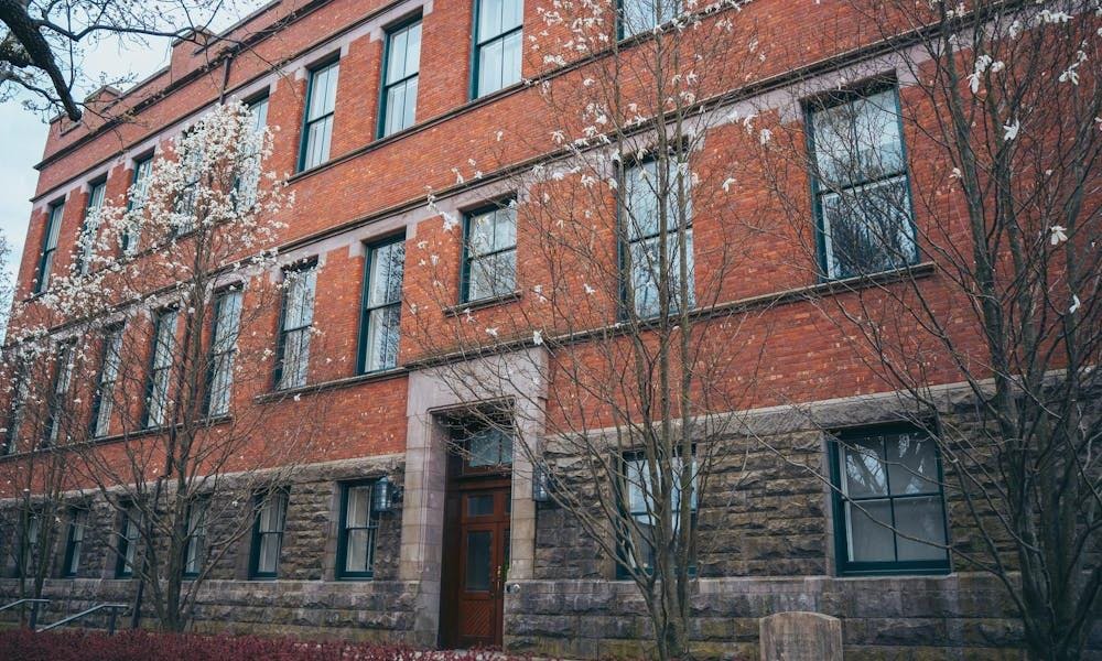 La foto muestra un edificio rojo con varios árboles desnudos en primer plano.