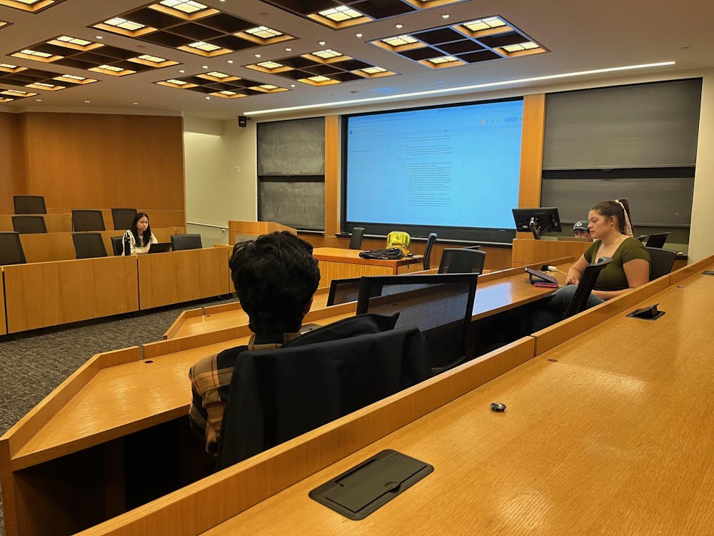 Four people sit in a meeting room and view a screen in the center of the room.