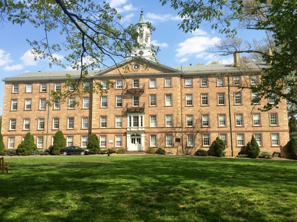 Light brick building with dozens of windows and white top of building.