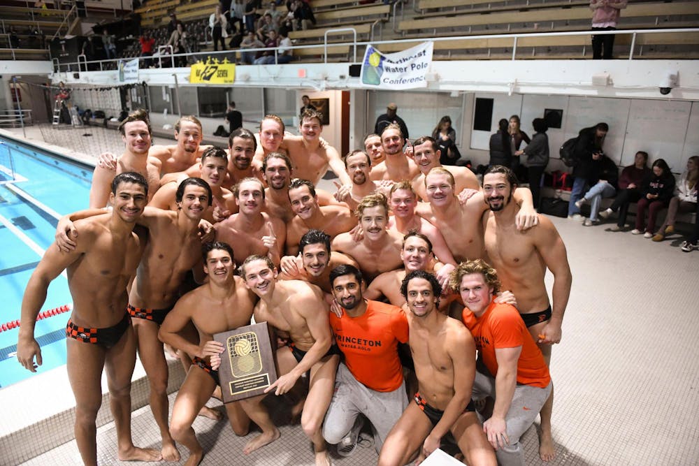 A group of men hugging one another whilst holding a winner's plaque outside a pool.