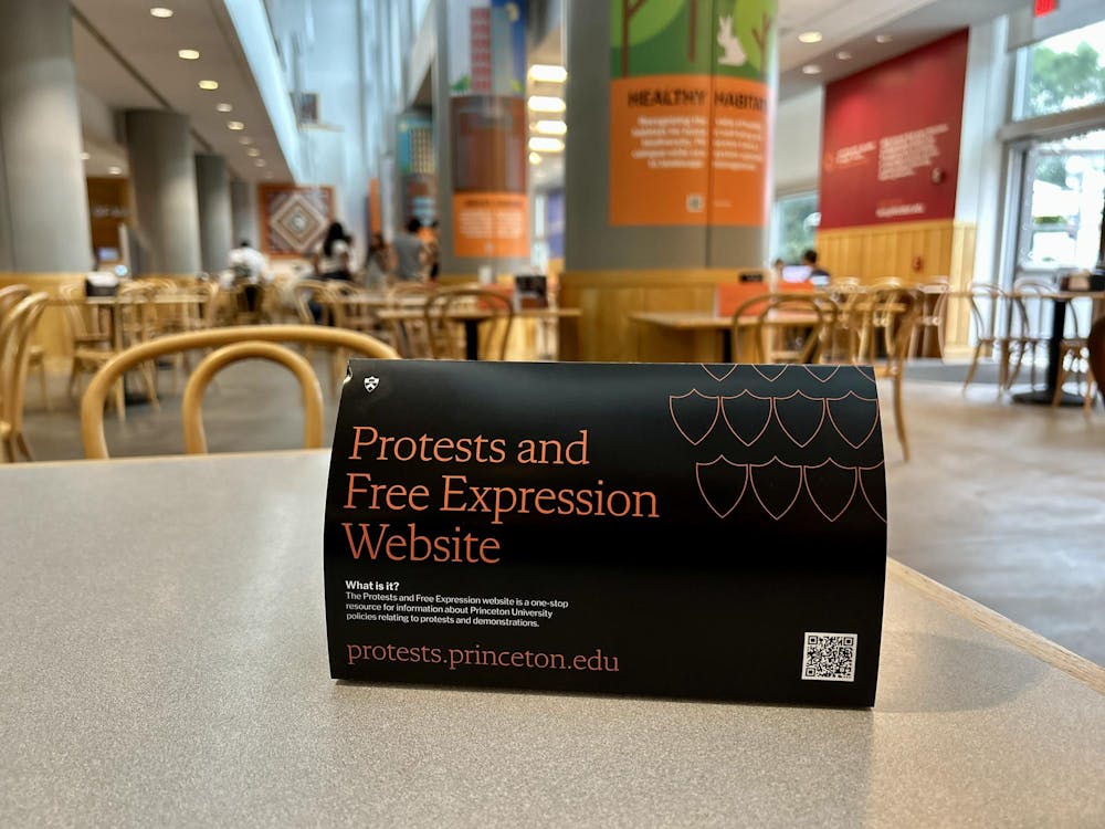 A folded paper reading "protests and free expression website" with a link to protests.princeton.edu and a QR code, atop a gray table