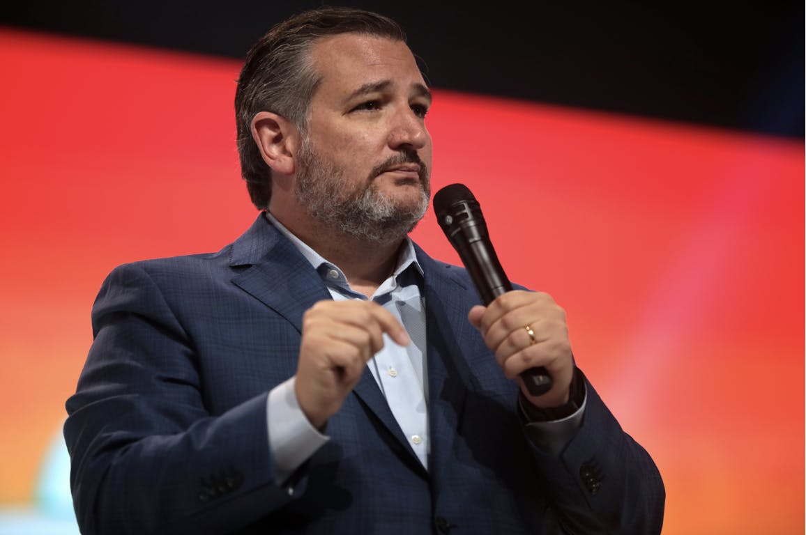 A man is holding a microphone while in front of a red background. 