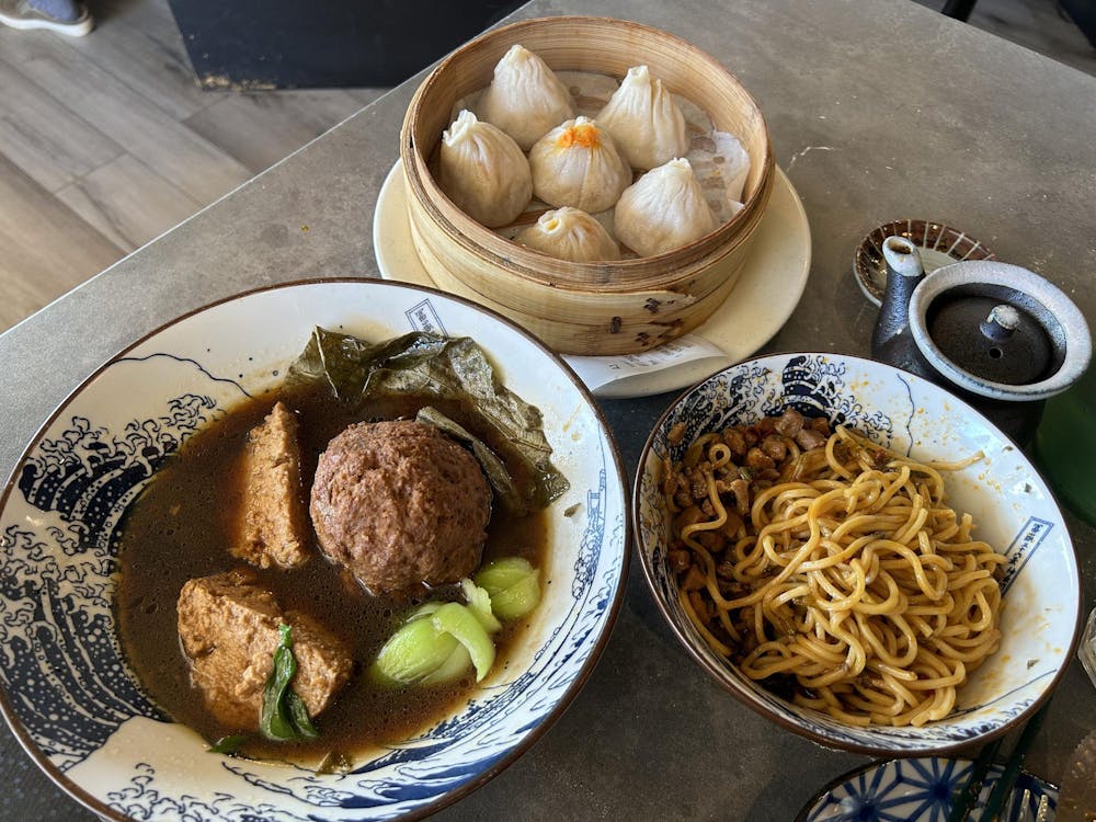 Three dishes, soup dumplings, scallion oil noodles, and jumbo meatballs, sit on a table.