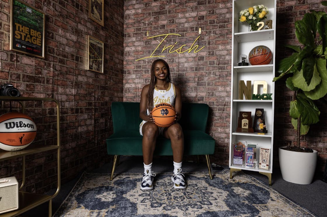 A woman holding a basketball and wearing a white jersey, sitting on a green couch.