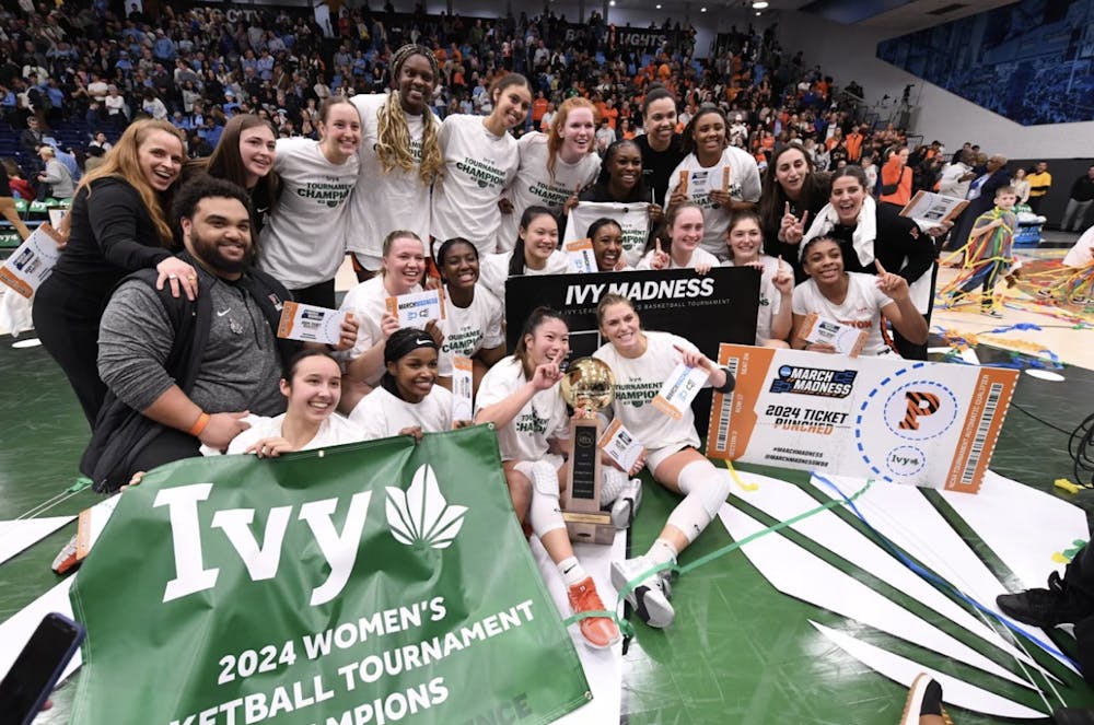 Group of women in white shirts on a basketball court posing with a banner, smiling, and celebrating.