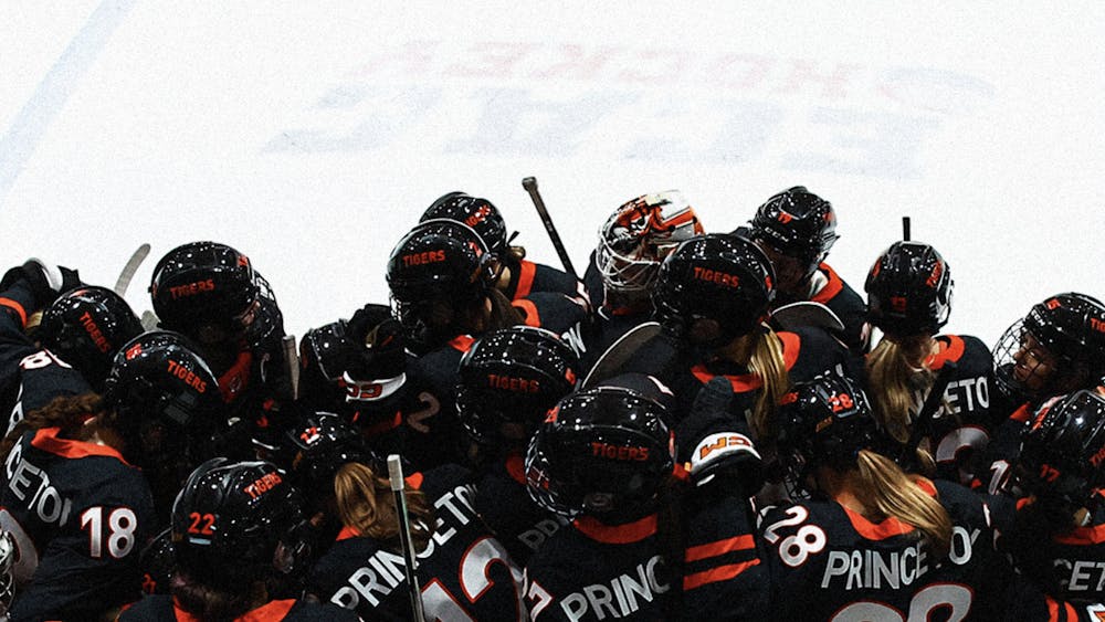Princeton women's ice hockey players in black jerseys together in big group on bench.