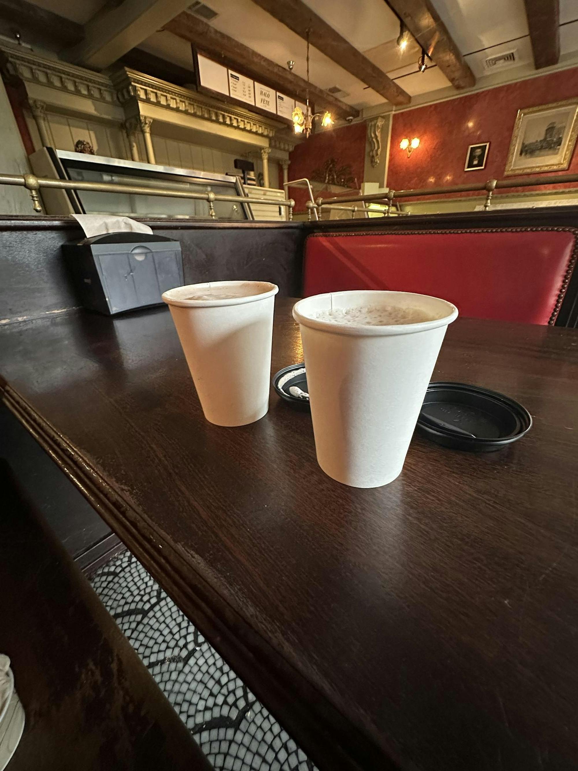 Two white paper cups on a brown table.