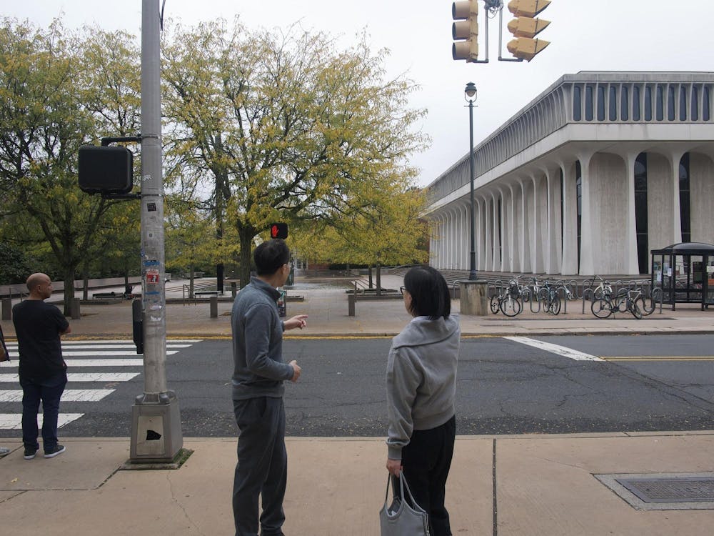 Two people stand in front of a crosswalk with a white building in the background.