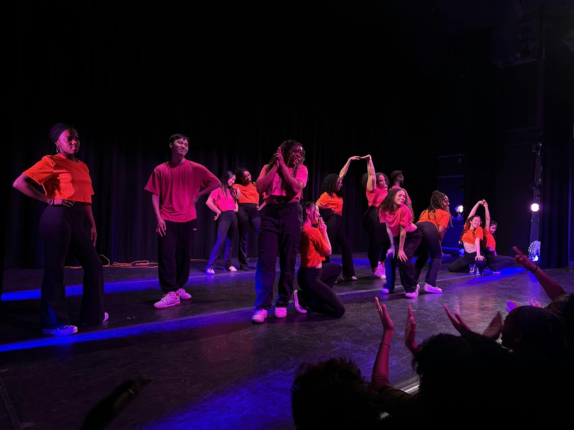 Dancers in pink and orange shirts do various poses on stage. 