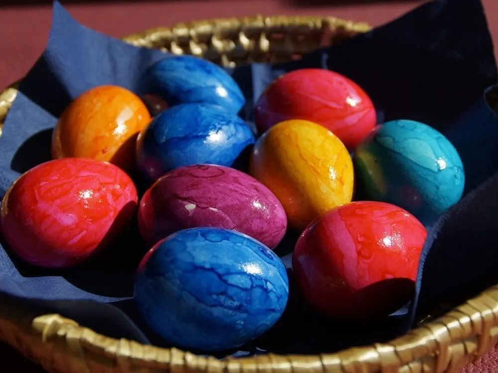 Blue, orange, red, and purple painted eggs on a blue napkin in a brown basket with a reddish-brown background.