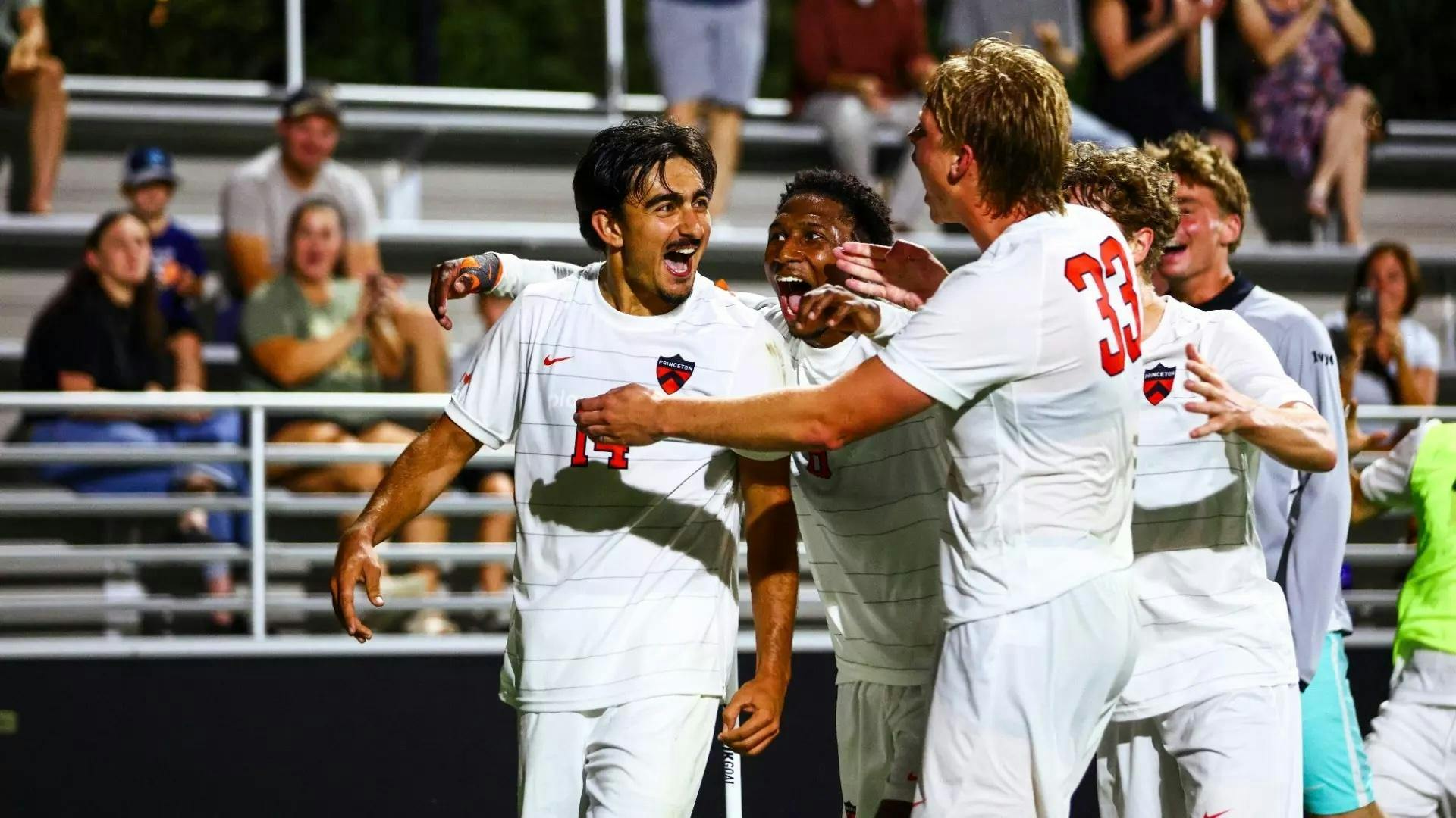 Four guys in white and orange jerseys celebrate a goal.