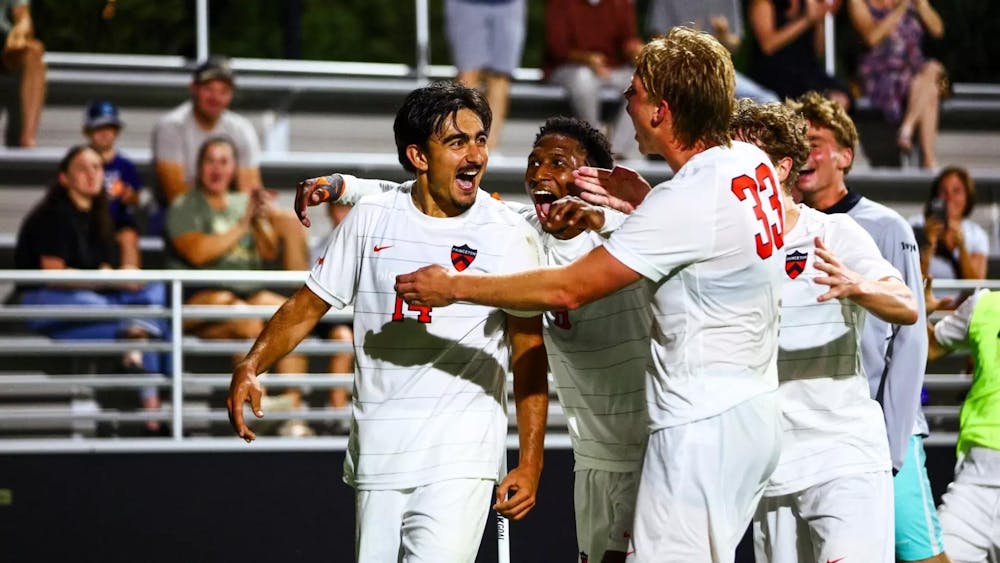 Four guys in white and orange jerseys celebrate a goal.